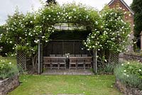 Wooden furniture in gazebo with climbing Rosa - The Flint House
