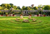 Double domed pergola in oak spans the garden dividing upper gravelled courtyards from the lower lawn featuring maze and central stones. The Collector Earl's Garden designed by Julian and Isabel Bannerman.