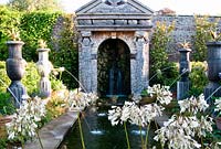 Rill pool flanked by turned oak urns spouting water through gilded lions' heads, with golden agaves in their tops. Water emerges from a rocky grotto framed by a scallop shell pediment and muscular caryatids. The Collector Earl's Garden designed by Julian and Isabel Bannerman.