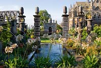 Rill pool flanked by turned oak urns spouting water through gilded lions' heads, with golden agaves in their tops. Oak columns with stylized acorns on the top frame a view of Oberon's Palace beyond. The Collector Earl's Garden designed by Julian and Isabel Bannerman. 