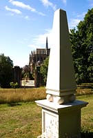 White obelisk with view down into the Collector Earl's Garden designed by Julian and Isabel Bannerman, with fountains featuring dogs' head spouts and oak domed pergola beyond. Behind is the dramatic form of Arundel Cathedral.