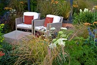 Modern wicker furniture on patio surrounded by Eryngium, Achilleas and grasses - 'The Landform Garden' - Gold medal winner and Best Summer Garden - RHS Hampton Court Flower Show 2012 