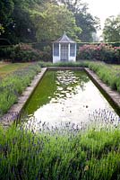 Blue and white summerhouse and formal lily pond edged with lavender
