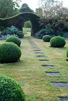 Slab path with box balls leading across lawn to yew arch in hedge