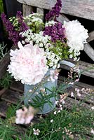 Bouquet of pink peony, purple sage and  cow parsley in a zinc can on a rustic wooden bench. In front Linaria purpurea 'Canon Went'