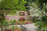 A wall mounted water fountain with metal basin and Osmunda regalis, Primula bullesiana and Viburnum plicatum - Germany