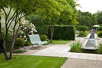 Formal designed garden with wooden bench, clipped trees and a rill. Plants include Amelanchier lamarckii, Buxus, Crambe cordifolia, Fagus, Iris pseudacorus and Vinca - Germany