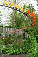 Colourful bladed curved sculpture and wall underplanted with perennials, ferns and grasses 