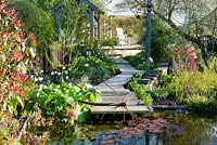 Pond with metal sculpture, decking and path with Narcissus poeticus