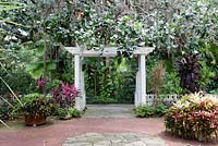 White wooden arbor, containers and plantings including Cordyline fruticosa 'Red Sister' Ti Plant, Bromeliads, Dracaena Marginata 'Tricolor' - Leu Gardens in Orlando, Florida