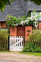 White gate to thatched cottage in summer 
