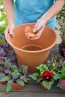 Step by step for planting colourful container - adding broken pieces of pot to aid drainage