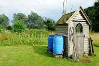 Small wooden garden shed with tools outside and blue plastic water butts