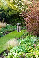 Modern sculpture and Spring border with Tulipa 'Recreado' and 'Spring Green'. Other plants include Stipa, Hellebores and Narcissus 'Thalia'
