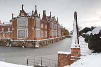 Large country house covered in snow in winter surrounded by frozen frosty moat. 