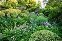 The walled herb garden features mounds of Phlomis fruticosa, variegated box and masses of herbs including purple sage, tansy, fennel, monkshood, Santolina, Alliums and pink flowering bistort, all lapping around a figurative bird bath. Beechenwood Farm, Odiham, Hants, UK