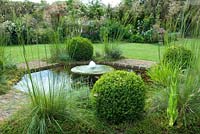 Millstone fountain surrounded by Buxus spheres and Stipa gigantea