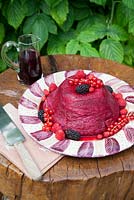 Summer Pudding decorated with fruit and coulis made by Lesley Wild on wood table in the garden.