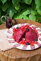 Summer Pudding decorated with fruit and coulis made by Lesley Wild on wood table in the garden.
