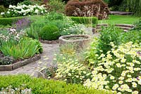 The sunken garden enclosed with Buxus curving hedges, with central antique stone trough raised pond water feature. Draught tolerant plants include Anthemis tinctoria, Erysimum 'Bowles' Mauve', Iris', Bergenias, Lavandula, Sage, Echinops, Artemesia and Achillea.