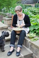 Lesley Wild shelling Broad Beans in the vegetable garden with Poppy the minature Schnauzer