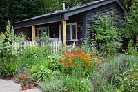 Garden room with decked garden. Densly planted border with Verbena bonariensis, Helenium,  Nepeta, Rose bush with hips and Lavandula. Pots of Pelargoniums.  