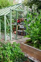 Greenhouse full of vintage tools, radio, hurricane lamp, and vase of Dahlias, in cutting garden with oak raised beds overflowing with Nicotiana sylvestris.
