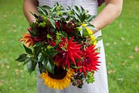 Large Autumnal multicoloured handtied bouquet with Sunflowers, Dahlias, Blackberries and Ivy foliage, held by Georgia Miles of The Sussex Flower School.
