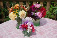 Flower arrangement with trio of Lathyrus latifolius - mixed Sweet Peas, mixed Dahlias and Verbena, Roses and Crocosmia in vintage glass vases on garden table.