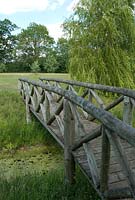 Wooden bridge over pond with long grass and a Willow tree at Wood Farm. June