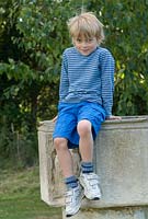 Boy sitting on the font in the garden where he was Christened. Wood Farm, June