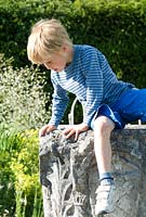Boy on the old stone well head in The White Garden, Wood Farm. June
