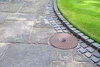 Stone slab path and cobble setts neatly surrounding drain and edging lawn