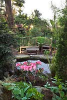 Pond in a woodland garden with rustic, hand made furniture. Planting includes Azalea, Convallaria majalis, Trillium and ferns - Seattle, USA