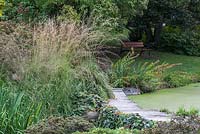 Grasses near a pond with path to bench hidden in shadow