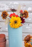 Simple floral arrangement of Zinnias, Rudbeckia 'Cherry Brandy' with Pennisetum in blue enamel container
