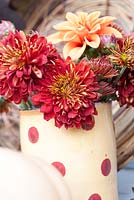 Autumn floral arrangement with chrysanthemums and dahlia in spotty jug with Squash 'Autumn Crown'