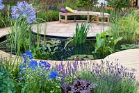 Central pond, surrounded by a decked path that leads to a seating area with sandstone paving and planting of Agapanthus, Cerinthe, Lavandula, Heuchera and Delphinium. 'A Taste of Ness' garden sponsored by Friends of Ness Gardens and designed by Phillippa Probert. RHS Tatton Flower Show 2012