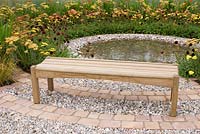 Wooden bench overlooking central rippling pool with spreading circles of pebbles, cobble setts, planting of Cosmos atrosanguineus and Achillea in the 'To The Beat' garden. Gold medal winner and Best Orchestra Garden - RHS Tatton Flower Show 2012