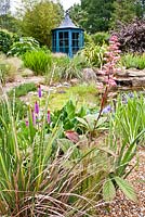 Pond area with gravel planting and blue painted gazebo, planting includes Rodgersia pinnata 'Maurice Mason', Primula vialii and Iris