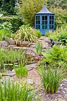 Pond area with gravel planting and blue painted gazebo, planting includes Kniphofia 'Dorset Sentry', Osmundo regalis, Phylostachys nigra and Phormium 'Yellow Wave'