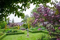 View of the garden with sundial in the centre of the lawn and Sambucus nigra 'Black Lace' in the foreground