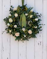 Christmas wreath hanging on white painted wooden door. Includes Rosa 'Artemis', Hypericum 'White Condor', Ivy and variegated Euonymus.