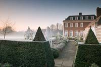 Formal garden in winter with Taxus - Yew hedges and  pyramid topiary, yorkstone path - Winfield House