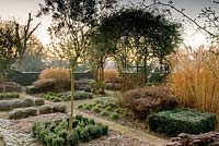 Formal garden in winter with Rosa growing over arch, Calamagrostis acutiflora, Buxus and yorkstone paving - Winfield House 
 