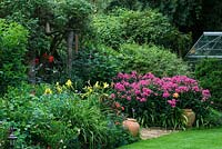 Wildlife conservation garden with borders of Hemerocallis, Phlox, Cerinthe and Dahlia flanking rustic arch 