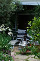 Garden furniture and white Agapanthus in pot on small patio in wildlife conservation garden 