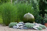 Backed by a Miscanthus group, water feature of granite sphere and shingles planted with Artemisia schmidtiana 'Nana' and Miscanthus sinensis