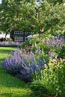 Bavarian country garden with perennial borders, roses and a bee house sheltered under old fruit trees