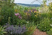 Bavarian country garden with perennials and a climbing arch with views to the countryside beyond 